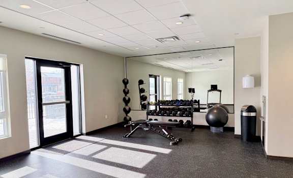 A spacious gym with a variety of equipment including dumbbells, a medicine ball, and a jump rope.