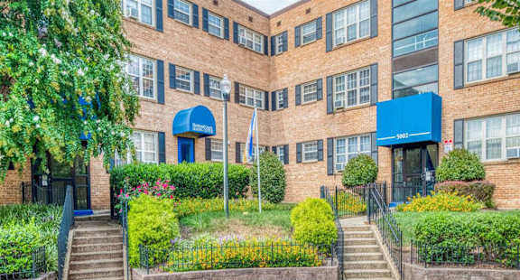 A building with a blue awning and a sign that reads "5000" is surrounded by greenery and a metal fence.