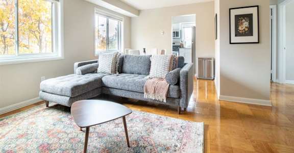 A grey couch with a pink throw blanket is in a room with a wooden floor and a large window.
