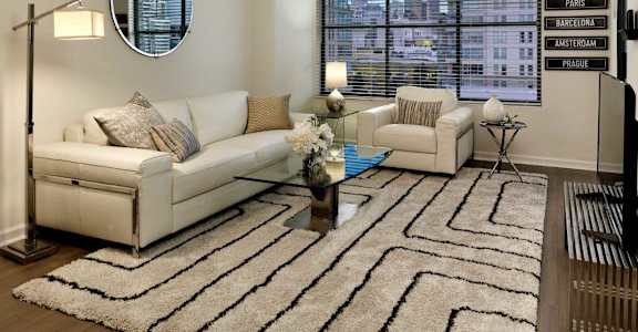 A living room with a white couch, a round mirror, and a rug with a black and white pattern.