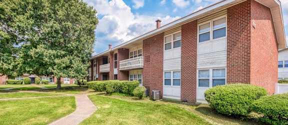 a brick apartment building with a sidewalk and green grass at Gates of West Bay in VA 23503
