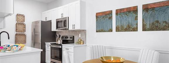A kitchen with a table and chairs in the foreground and a painting on the wall.