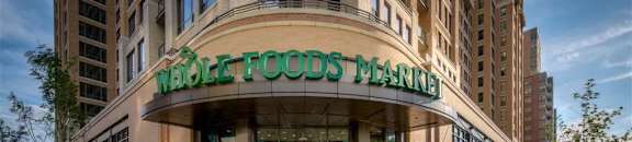 A Whole Foods Market is bustling with activity as people walk around the entrance.