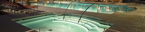 Illuminated hot tub and pool, outdoor furniture, and cabanas at night at CHANDLER APARTMENT HOMES, Las Vegas, NV