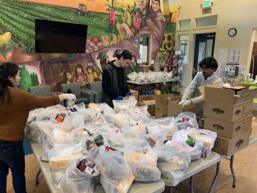 Mutual Housing staff organize bags of food on folding tables in the Spring Lake community room