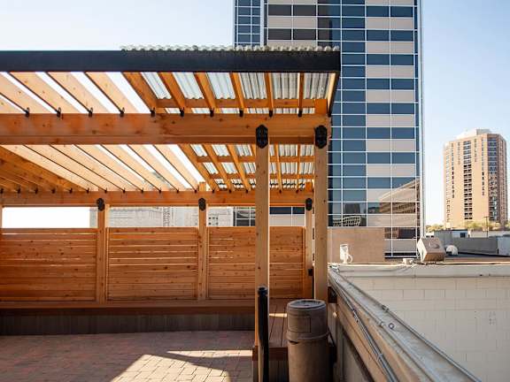 A wooden pergola with blue cushioned chairs and a table with flowers on it.