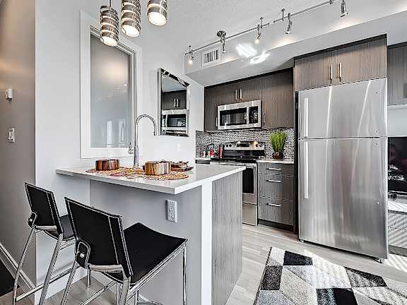 A modern kitchen with a stainless steel refrigerator, a white countertop, and black barstools.