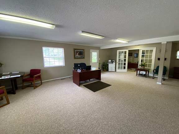 A room with a desk, chairs, and a framed picture on the wall.