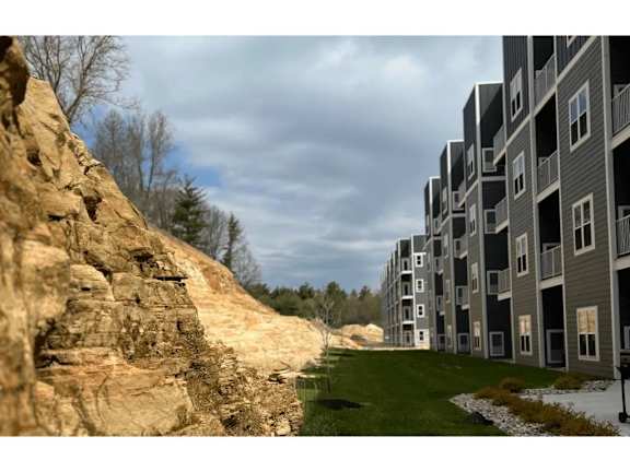 A large rock formation is in the foreground of a grassy area with apartment buildings in the background.