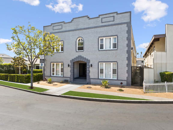 the front of a grey brick house with a driveway and a tree