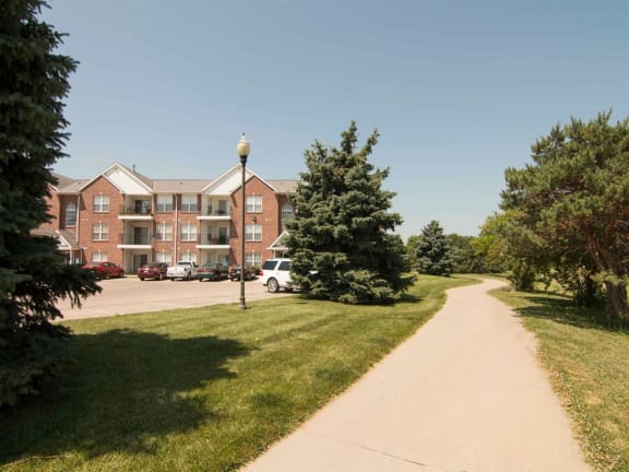 a sidewalk in front of an apartment building with trees and grass