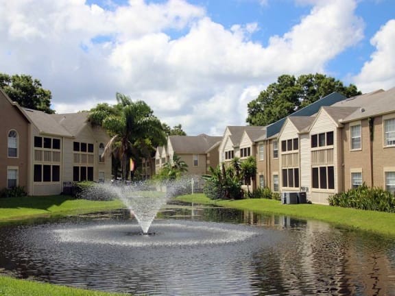 a fountain in the middle of a pond with apartment buildings in the background