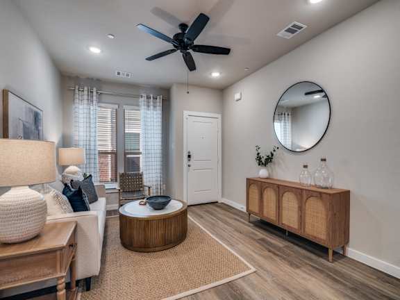 A living room with a ceiling fan, a round mirror, and a wooden cabinet.
