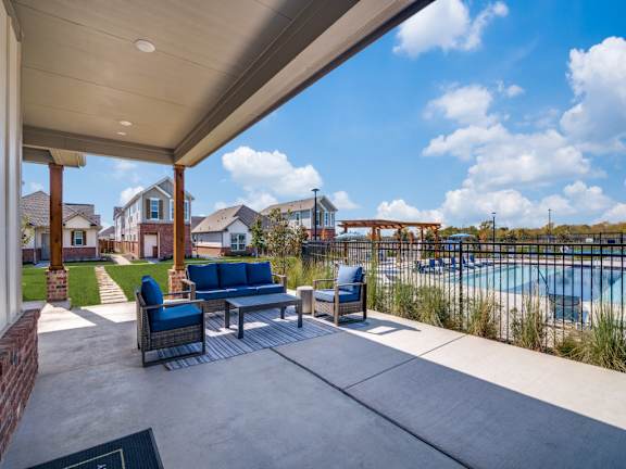 A patio with a couch and chairs overlooking a pool.