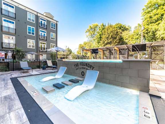 a pool with two lounge chairs in front of an apartment building at The Foundry, South Bend, IN