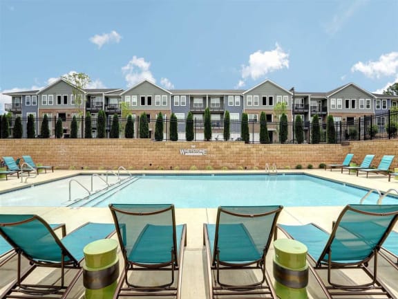 a swimming pool with lounge chairs in front of apartment buildings