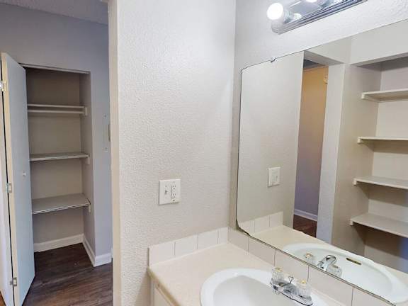 A white bathroom with a sink, mirror, and shelves.