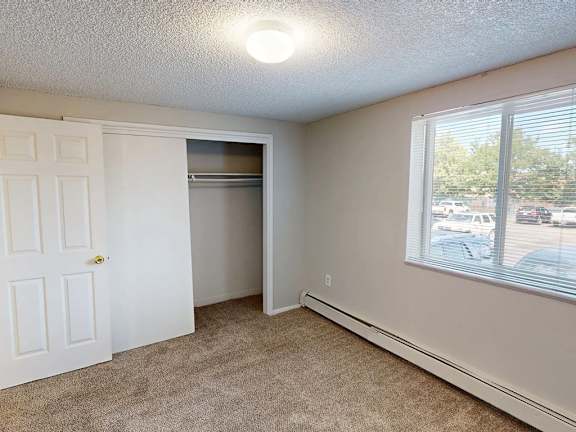 A room with a white door, carpeted floor, and a window showing a parking lot outside.