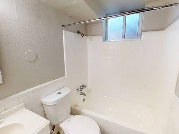 A white toilet is in a small bathroom with a white tub and sink.