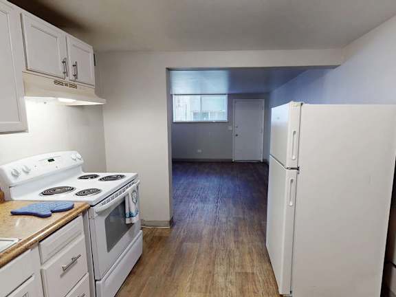 A kitchen with white appliances and wooden floors.