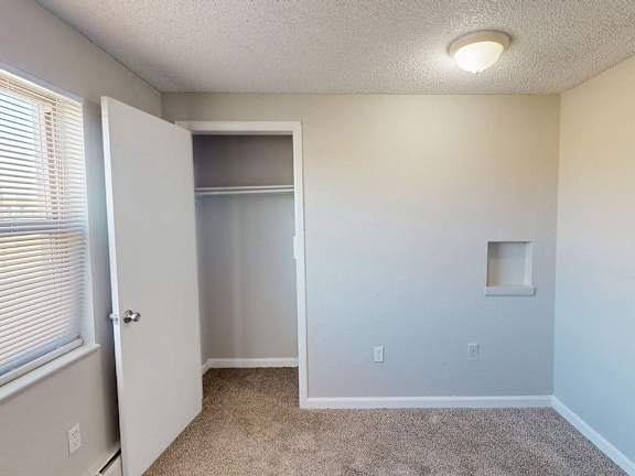 A room with a carpeted floor and a small window with blinds.