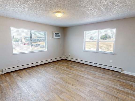 A room with wood flooring and two windows.