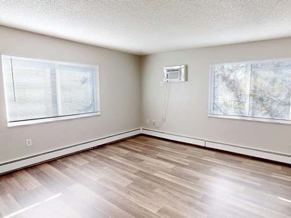A room with wooden flooring and two windows.