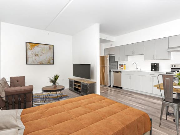 a living room with an orange bed and a kitchen with white cabinets