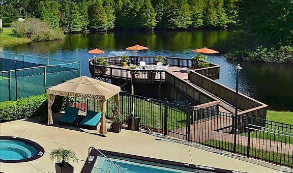 A pool area with a hot tub and a deck overlooking a lake.