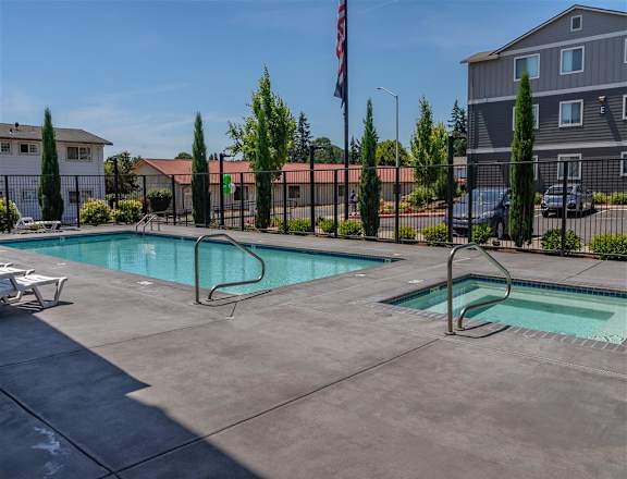 A pool with a diving board in the foreground and a flag in the background at St Helens Place Apartment Homes, St Helens, OR