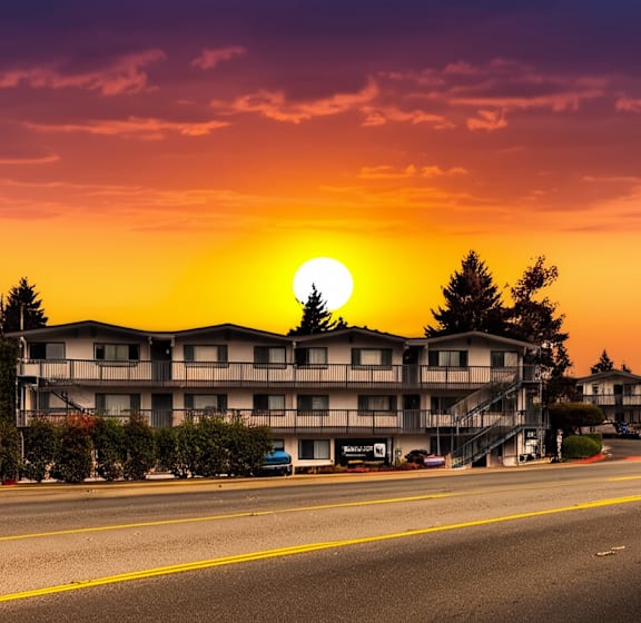 A sunset view of a street with apartment buildings and cars parked on the side.