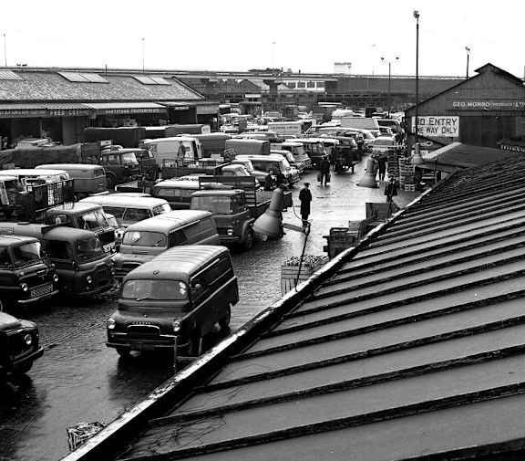 A black and white photo of a train station with many cars and trucks.