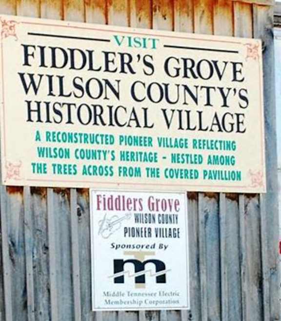 A sign for Fiddler's Grove Wilson County's Historical Village is displayed on a wooden fence. at Venue at 109 Apartments, Lebanon , TN, 37090