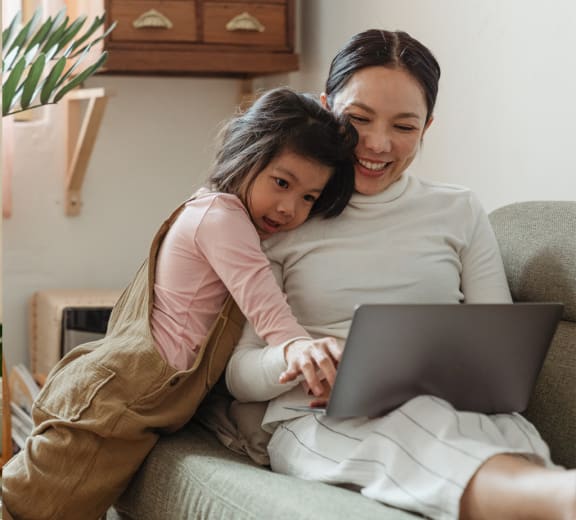 a mother and daughter sitting on a couch looking at a laptop