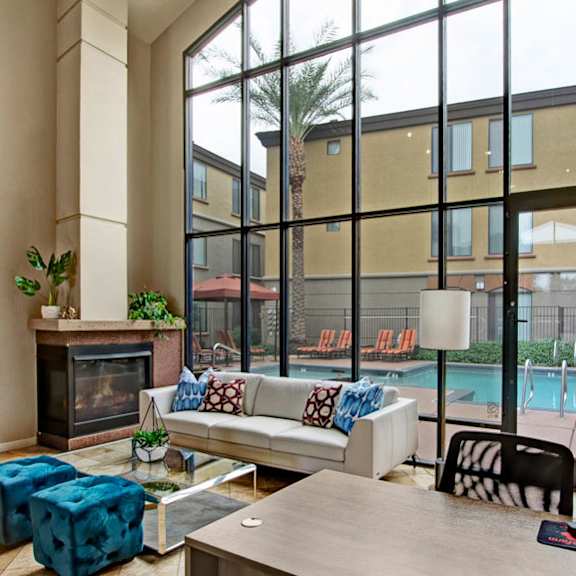 A common room with couches, a desk, a fireplace, chairs, stools, a coffee table, and a door to the pool area at Bolero Apartments. 