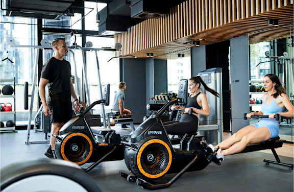 A gym with people exercising and a rowing machine in the foreground.