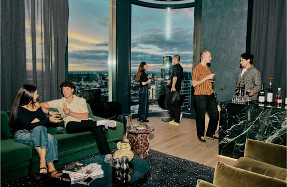 A group of people are gathered in a room with a large window overlooking a cityscape.