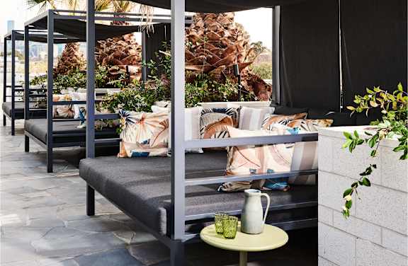 A patio with a couch, a table with a pitcher and glasses on it, and a pineapple tree in the background.