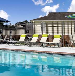 A pool with chairs and umbrellas in front of a building.