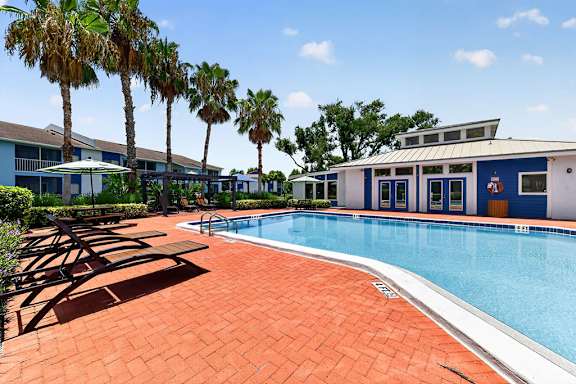 A pool surrounded by palm trees and a building.