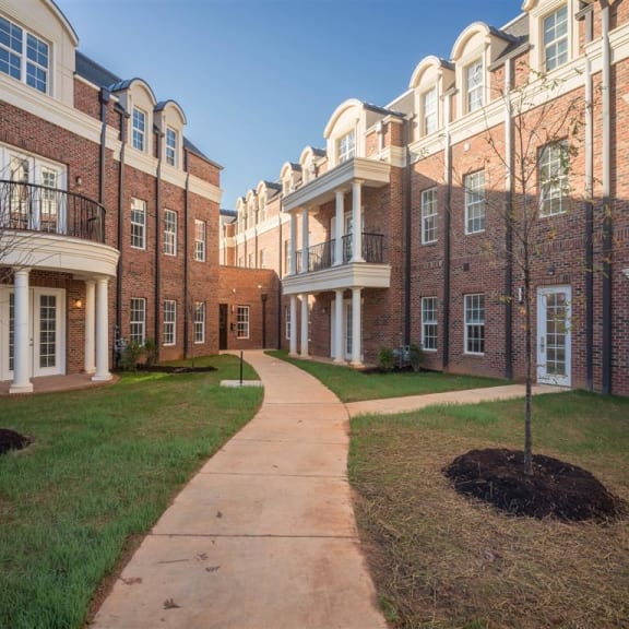 Three-story brick residential building at Tindall Park Apartments featuring classic architecture, balconies, and a landscaped courtyard.