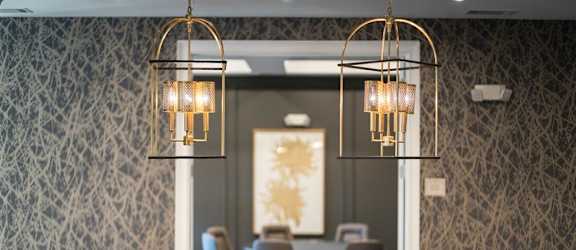 A dining areStylish dining space at Tindall Park Apartments with modern lighting, dark wood furniture, and elegant wallpaper.a with woven-back chairs, chandeliers, and built-in shelving.