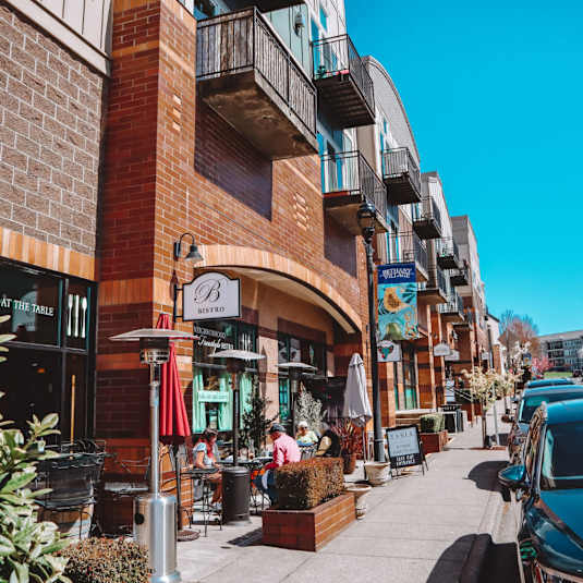 A street view of a sunny day with people sitting outside a restaurant.
