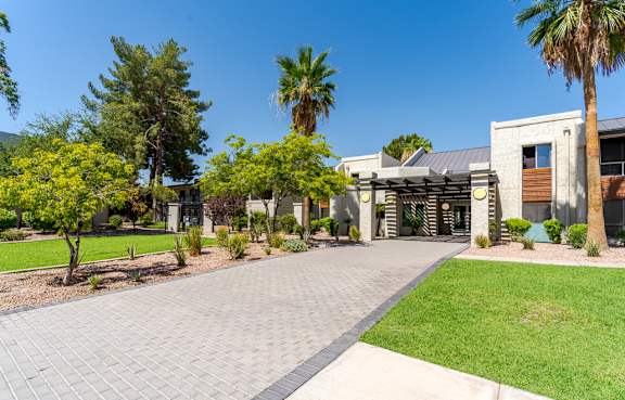 A paved walkway leads to the Sono Tempe Apartments leasing office, featuring a modern building, covered entrance, palm trees, and desert landscaping.