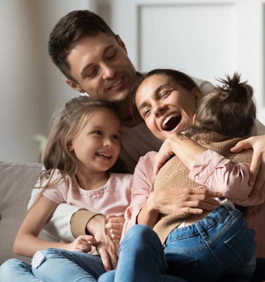 A family of three is sitting closely together on a couch.