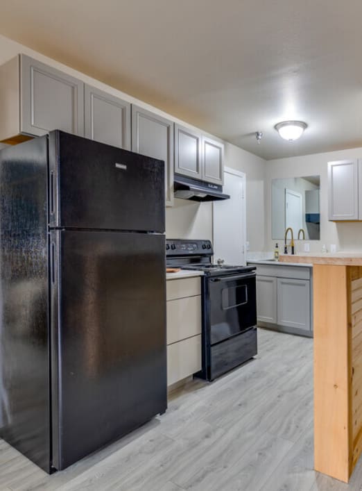 a living room with a couch a table and a chair and a kitchen with a refrigerator andat The Lodge Apartments, Tulsa, 74129
