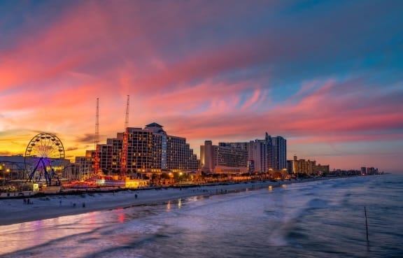Shoreline of Daytona Beach, Florida with waves on sand, amusement park, and large hotels at dusk