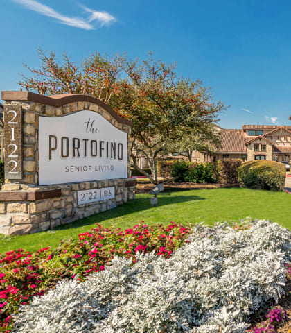 the entrance to the portofino senior living community with a sign and flowers