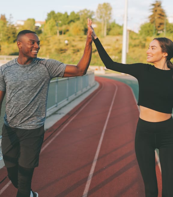 A man and a woman are high-fiving each other on a running track.