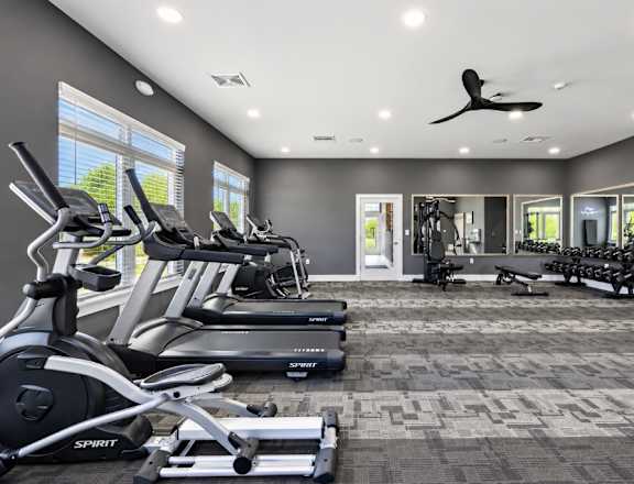 A spacious gym with treadmills, elliptical machines, and a fan.